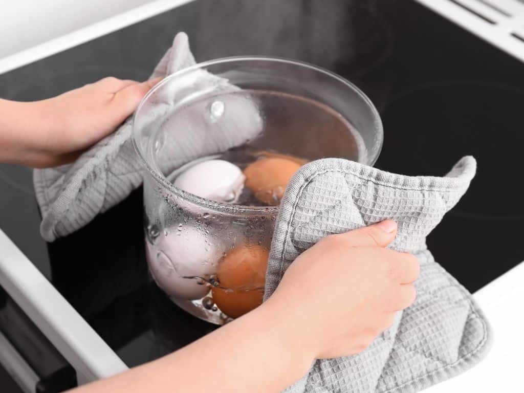 Boiled eggs cooking in a glass pot on a cooktop.